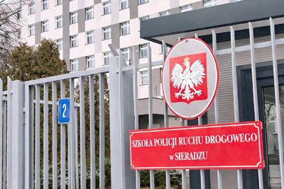 Tablica urzędowa z napisem Szkoła Policji Ruchu Drogowego w Sieradzu wraz godłem państwowym.