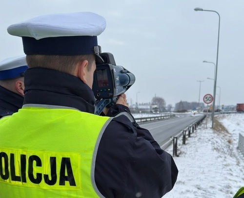 Policjant ruchu drogowego rejestrujący prędkość pojazdów w trakcie zajęć praktycznych.