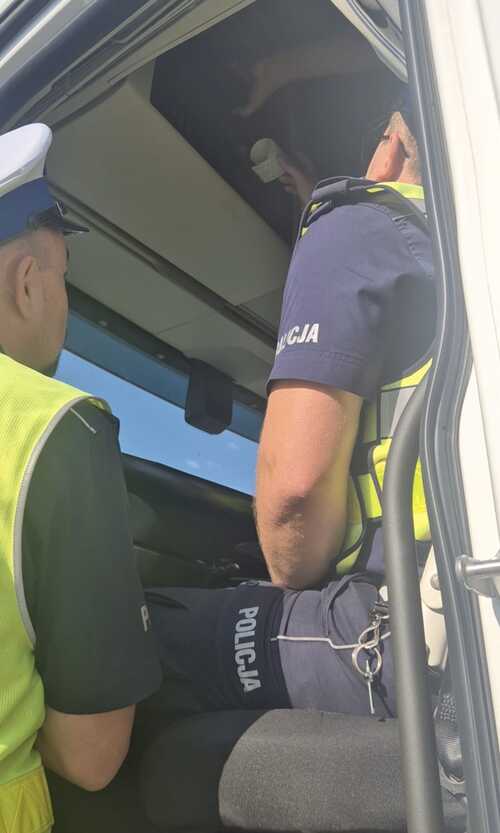 Na zdjęciu są widoczni słuchacze Szkoły Policji Ruchu Drogowego w Sieradzu, którzy w ramach zajęć praktycznych przeprowadzają kontrolę pojazdu ciężarowego wyposażonego w tachograf.