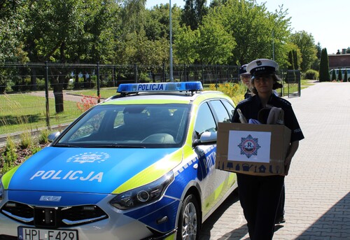 Na zdjęciu widoczna funkcjonariuszka Szkoły Policji Ruchu Drogowego niosąca paczkę.